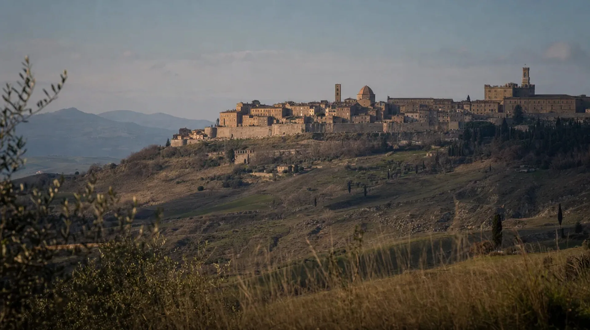 The walled hill town of Volterra rising above the Tuscan countryside, its stone ramparts catching low afternoon light